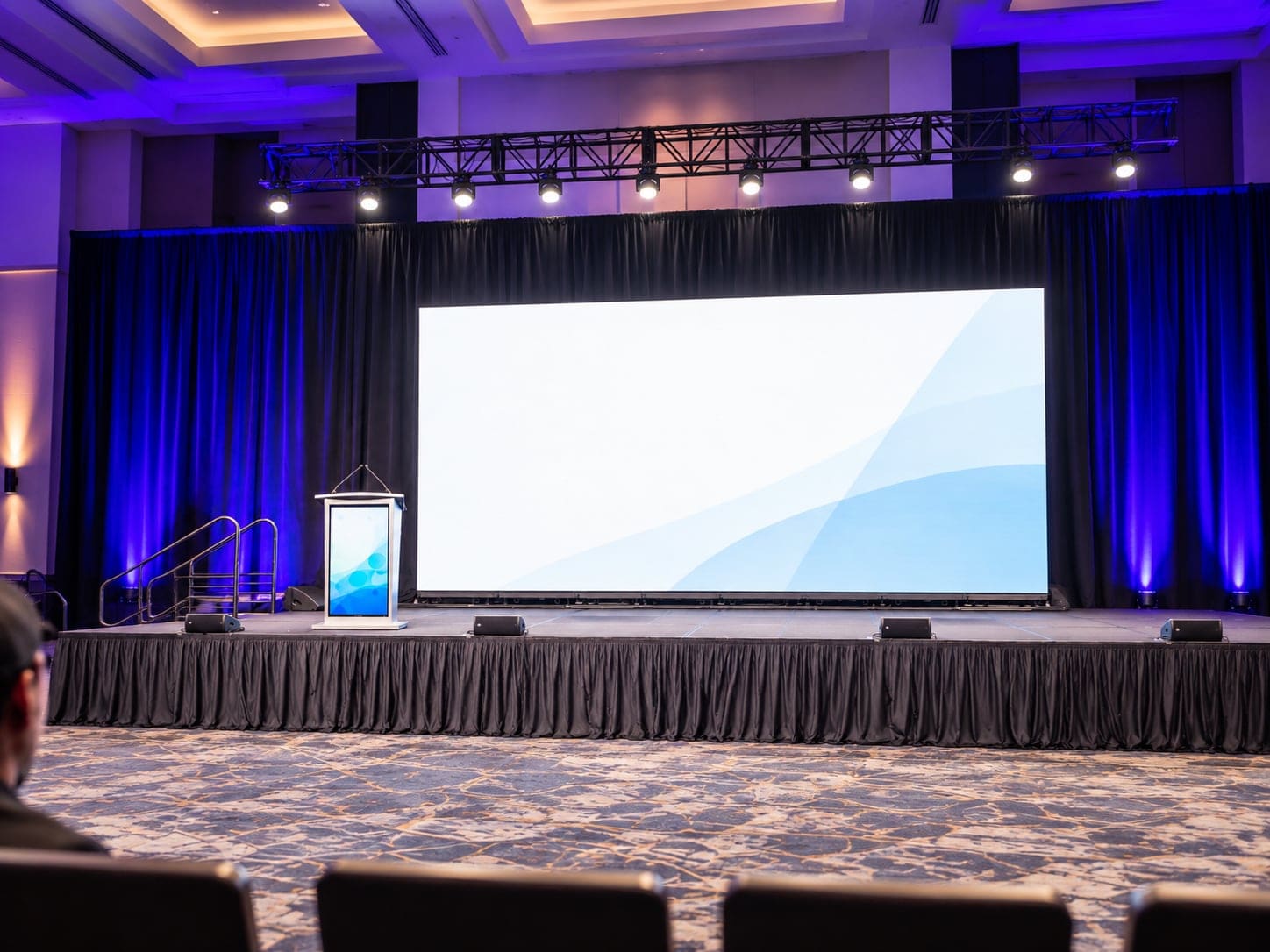 Event stage with a podium showing an audience-facing LED screen, beside a large rear screen