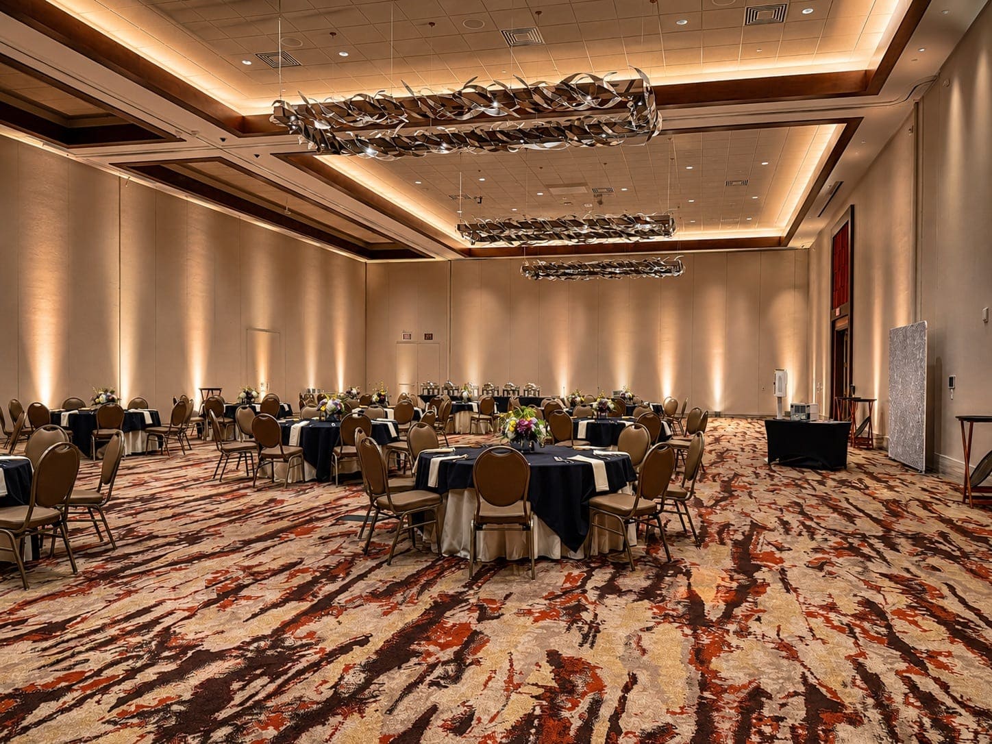 Ballroom set for dinner with warm amber uplighting and sculptural overhead fixtures